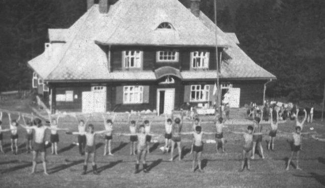 czarno-białe zdjęcie grupy dzieci przed budynkiem ćwiczących gimnastykę